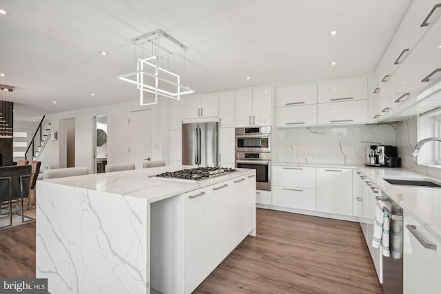 kitchen with light wood-type flooring, appliances with stainless steel finishes, white cabinetry, sink, and a kitchen island