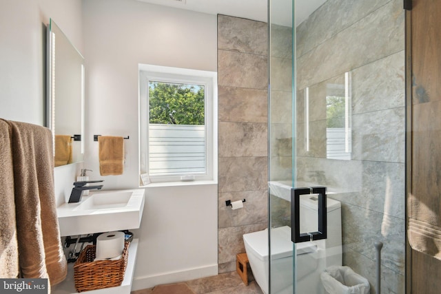 bathroom featuring baseboards, a tile shower, a sink, and tile patterned floors