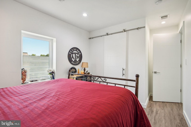 bedroom featuring a barn door, recessed lighting, wood finished floors, visible vents, and baseboards