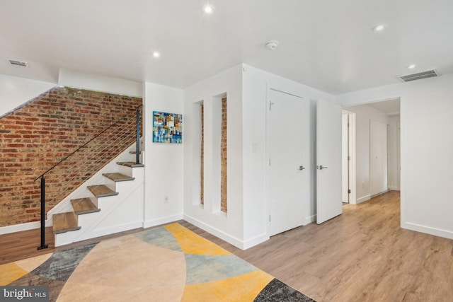 entrance foyer with brick wall, light wood-style flooring, stairway, and visible vents