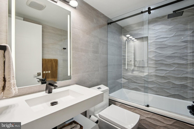 bathroom with toilet, shower / bath combination with glass door, tile walls, and a sink