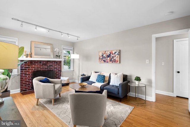 living room with light wood-type flooring, a brick fireplace, and rail lighting