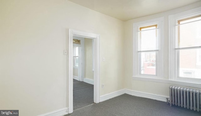 empty room with dark colored carpet, baseboards, and radiator heating unit