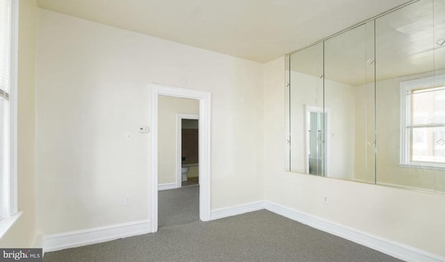 spare room with baseboards and dark carpet