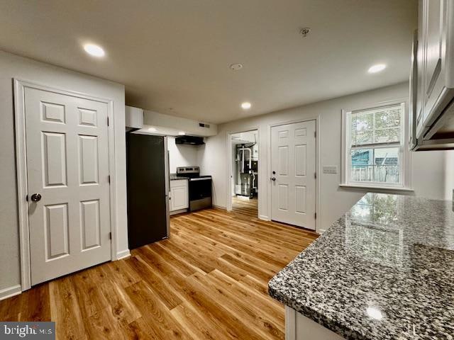 kitchen featuring light wood-type flooring, white cabinets, appliances with stainless steel finishes, and dark stone counters