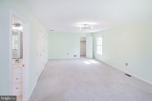 unfurnished bedroom with baseboards, light carpet, and a walk in closet