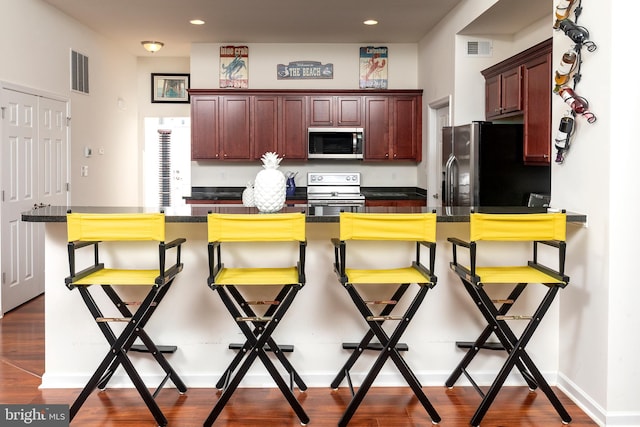 kitchen with dark wood-type flooring, a kitchen breakfast bar, and appliances with stainless steel finishes