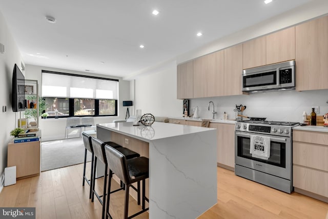 kitchen with appliances with stainless steel finishes, light stone counters, a center island, light hardwood / wood-style floors, and a breakfast bar area