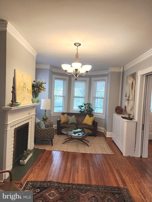 living room featuring radiator, ornamental molding, a brick fireplace, hardwood / wood-style flooring, and an inviting chandelier