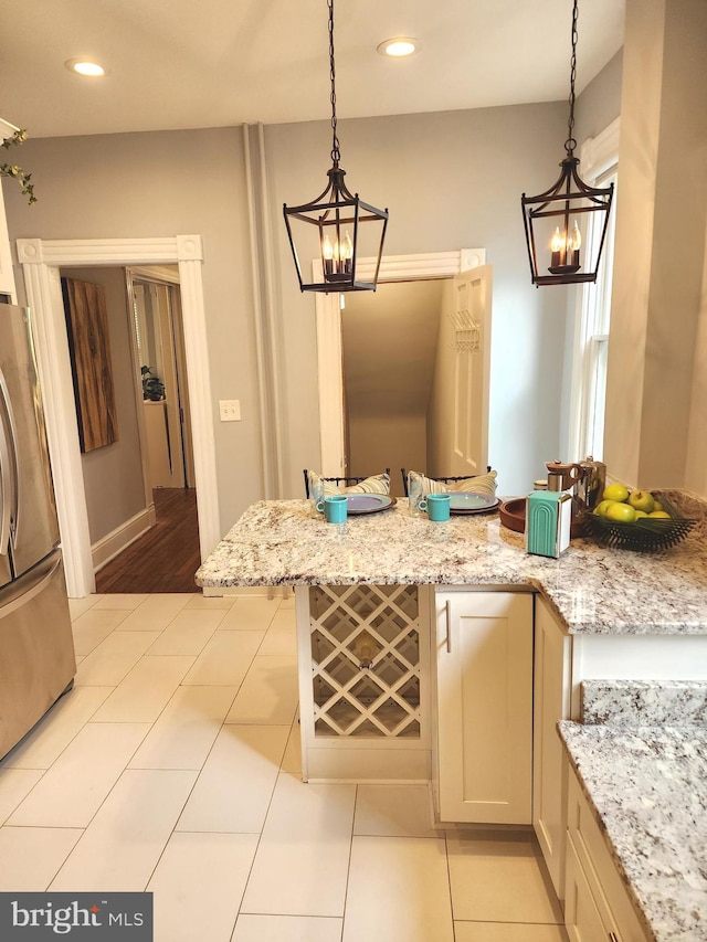 kitchen with pendant lighting, an inviting chandelier, light stone countertops, and stainless steel fridge