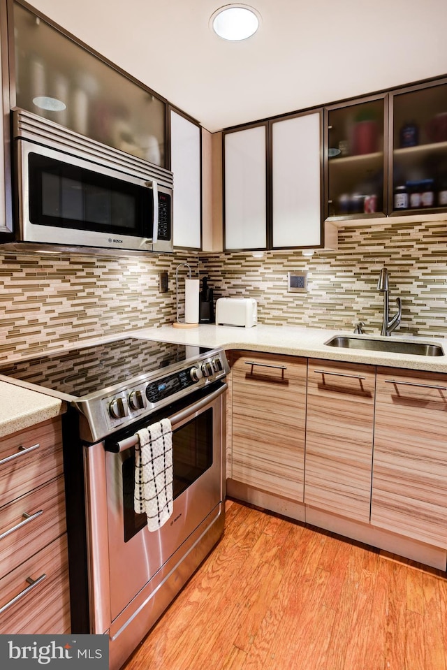 kitchen with light wood-style flooring, appliances with stainless steel finishes, backsplash, and a sink