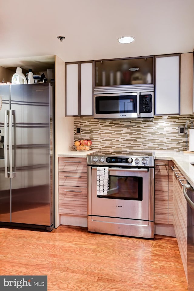 kitchen featuring stainless steel appliances, light countertops, light wood-style flooring, decorative backsplash, and modern cabinets