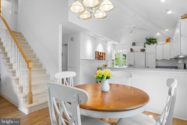 dining area with light hardwood / wood-style flooring, ceiling fan with notable chandelier, beamed ceiling, and high vaulted ceiling