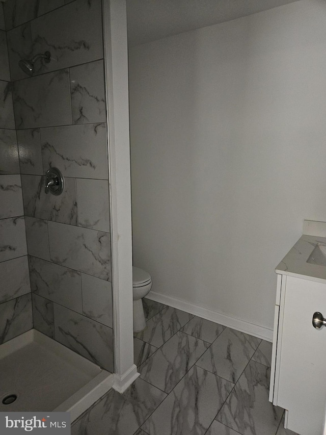 bathroom featuring toilet, vanity, baseboards, marble finish floor, and a shower stall