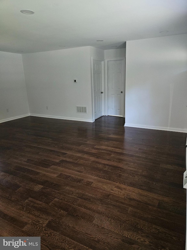 empty room featuring visible vents, dark wood finished floors, and baseboards