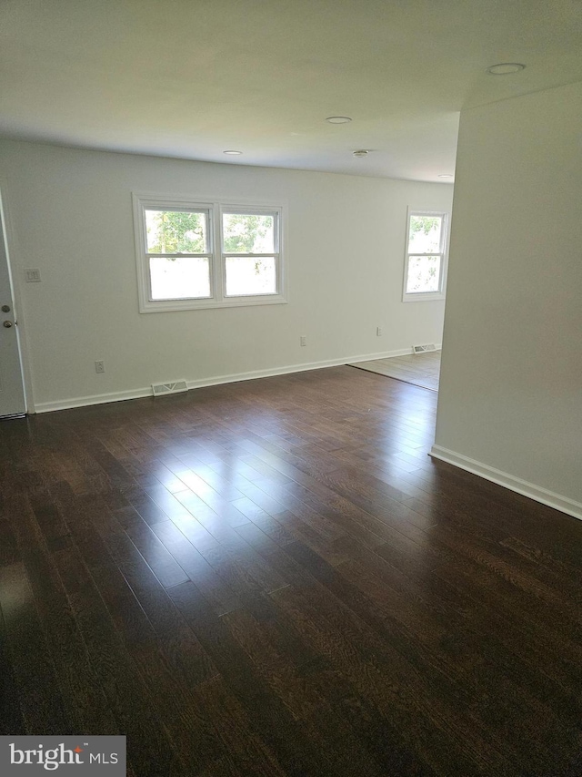 empty room with dark wood-style floors, visible vents, and baseboards