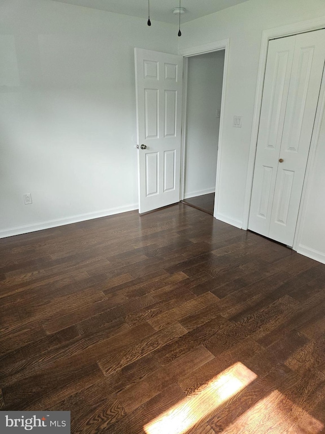 unfurnished bedroom with dark wood-style floors, baseboards, and a closet