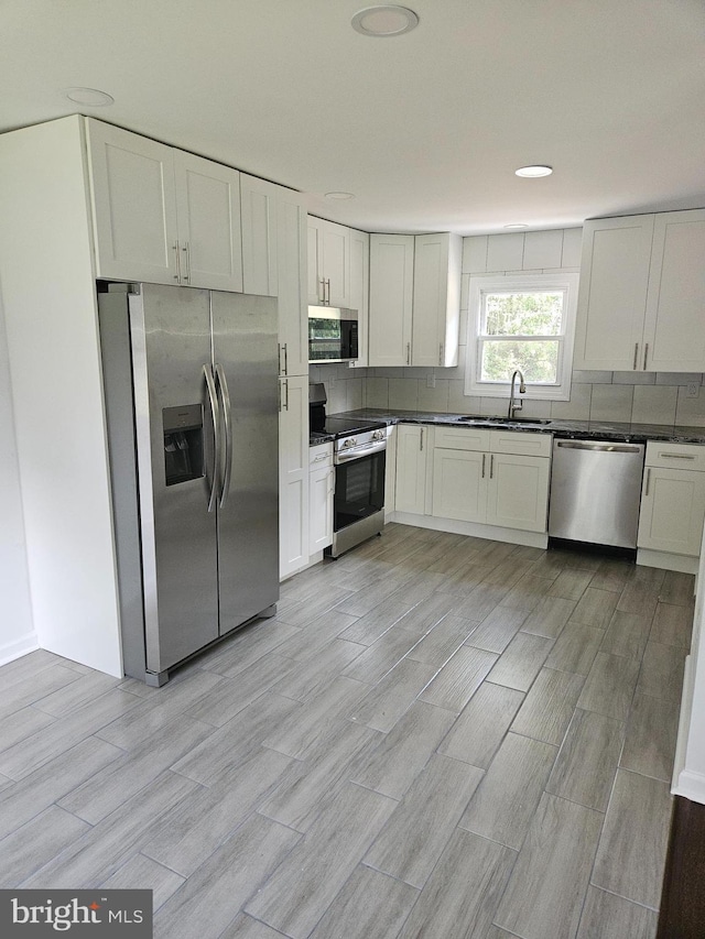 kitchen with stainless steel appliances, dark countertops, a sink, and decorative backsplash