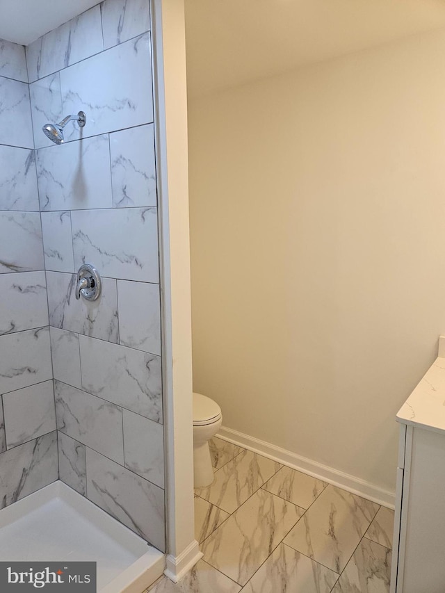 bathroom with marble finish floor, baseboards, a tile shower, and vanity