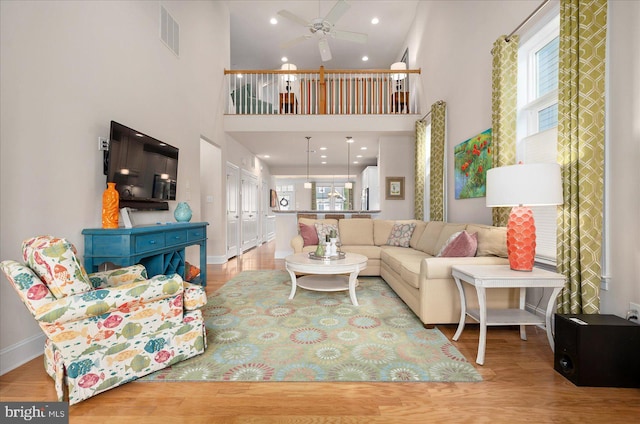 living room featuring plenty of natural light, ceiling fan, a high ceiling, and light hardwood / wood-style floors