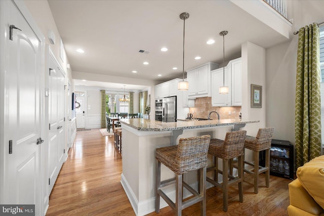 kitchen featuring light stone counters, decorative light fixtures, kitchen peninsula, and light hardwood / wood-style floors