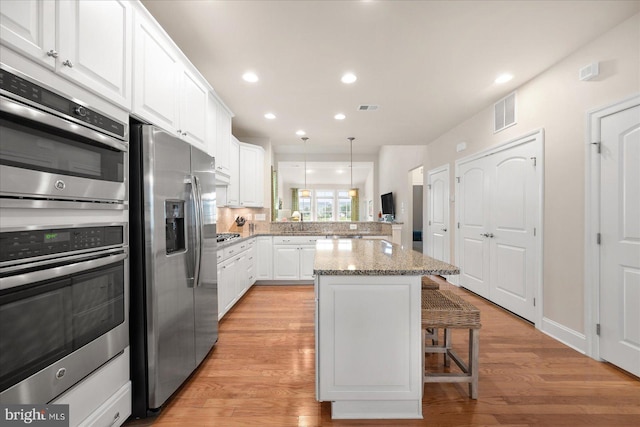 kitchen featuring decorative light fixtures, kitchen peninsula, a breakfast bar, appliances with stainless steel finishes, and light hardwood / wood-style floors