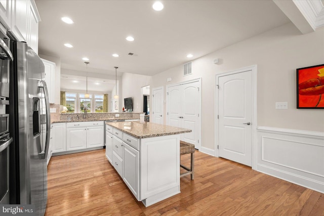 kitchen featuring white cabinets, light stone countertops, light hardwood / wood-style floors, stainless steel refrigerator with ice dispenser, and pendant lighting