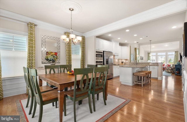 dining area with ornamental molding, an inviting chandelier, and light hardwood / wood-style floors