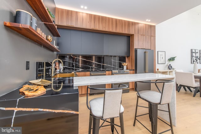 kitchen with appliances with stainless steel finishes, a kitchen bar, light hardwood / wood-style floors, and stone countertops