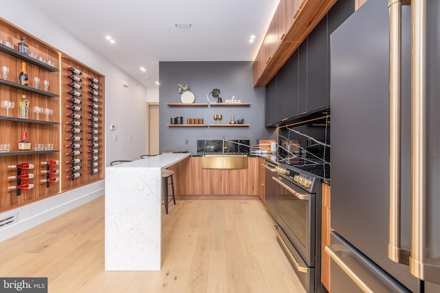 kitchen with stainless steel appliances, kitchen peninsula, sink, stone countertops, and light hardwood / wood-style floors