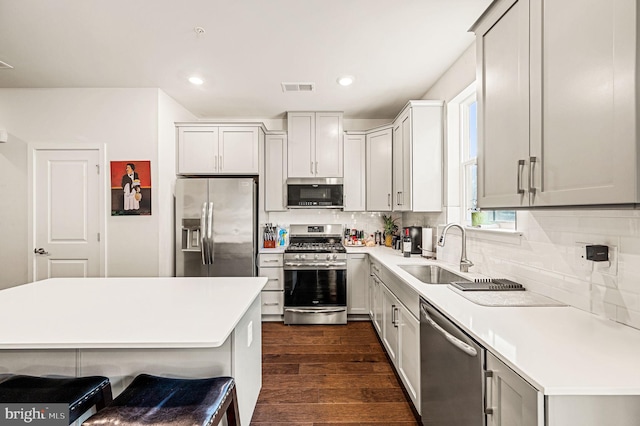 kitchen with appliances with stainless steel finishes, dark hardwood / wood-style flooring, sink, a kitchen breakfast bar, and tasteful backsplash