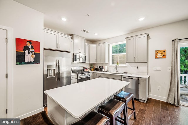 kitchen featuring appliances with stainless steel finishes, sink, dark wood-type flooring, a kitchen island, and decorative backsplash