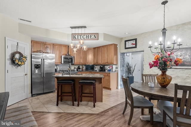 kitchen featuring pendant lighting, a kitchen island with sink, stainless steel appliances, and light wood-type flooring