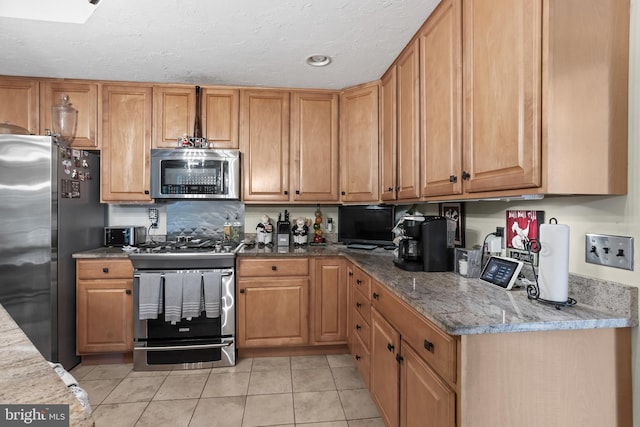 kitchen featuring light stone countertops, light tile patterned flooring, appliances with stainless steel finishes, and a textured ceiling