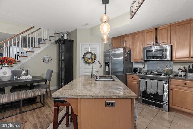 kitchen with hanging light fixtures, dark stone countertops, stainless steel appliances, a center island with sink, and sink