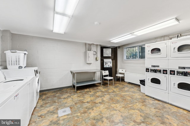 community laundry room with stacked washer / drying machine, concrete block wall, and washing machine and clothes dryer