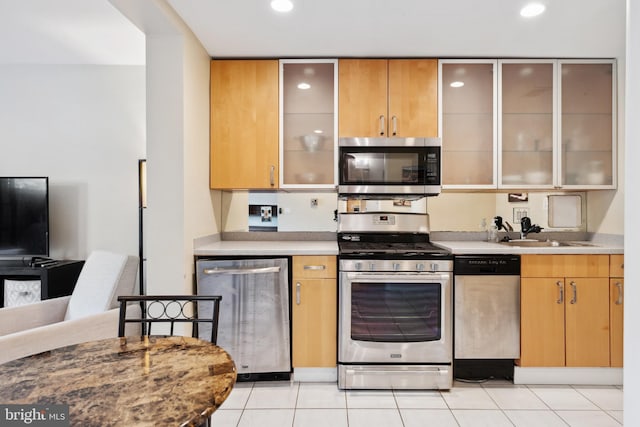 kitchen with glass insert cabinets, stainless steel appliances, a sink, and light countertops