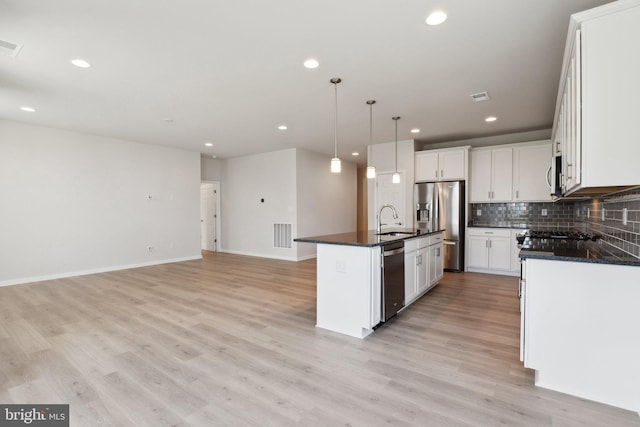 kitchen with decorative backsplash, an island with sink, stainless steel appliances, light wood-type flooring, and a sink