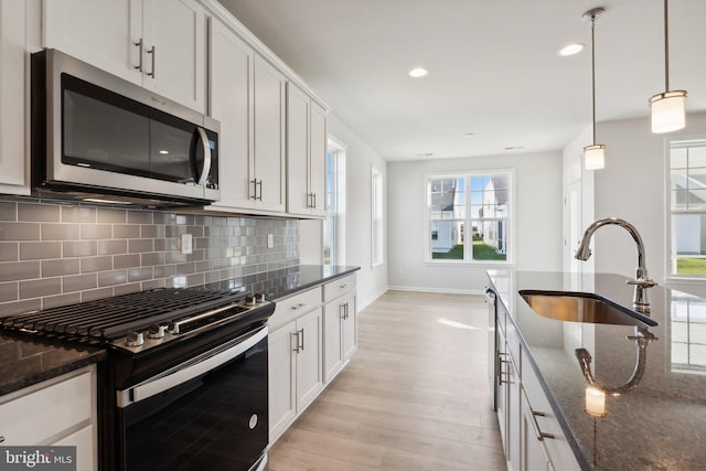 kitchen featuring dark stone counters, gas range, stainless steel microwave, a sink, and backsplash