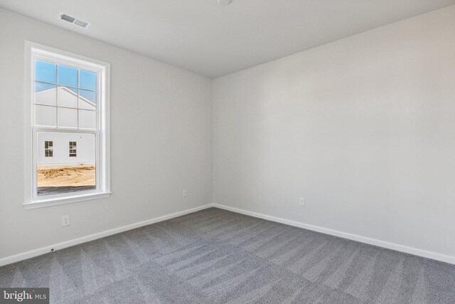 empty room with dark carpet, visible vents, and baseboards