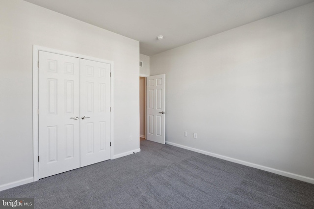 unfurnished bedroom with baseboards, dark carpet, and a closet