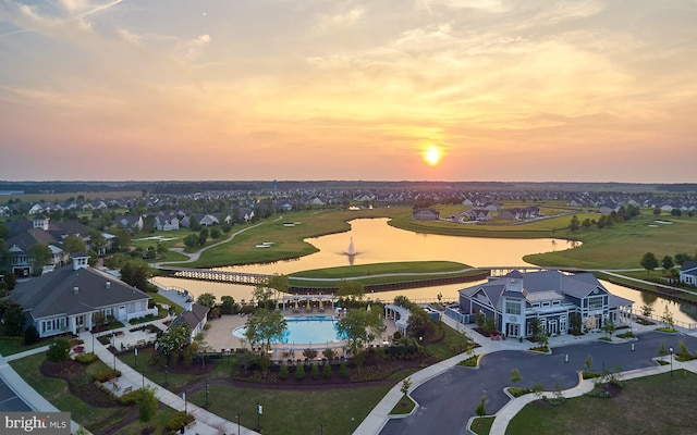 aerial view at dusk featuring a water view, view of golf course, and a residential view