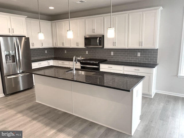 kitchen featuring light hardwood / wood-style flooring, stainless steel appliances, a center island with sink, pendant lighting, and white cabinetry