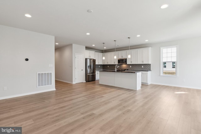 kitchen with appliances with stainless steel finishes, dark countertops, open floor plan, and visible vents