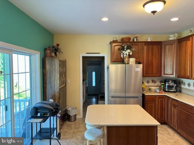 kitchen with tasteful backsplash, a kitchen island, stainless steel refrigerator, and light tile patterned flooring