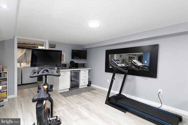 workout room featuring light wood-style flooring, wine cooler, baseboards, and washing machine and clothes dryer