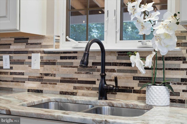 room details with white cabinets, tasteful backsplash, light stone counters, and sink