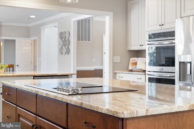 kitchen with white cabinetry, ornamental molding, light stone counters, and appliances with stainless steel finishes