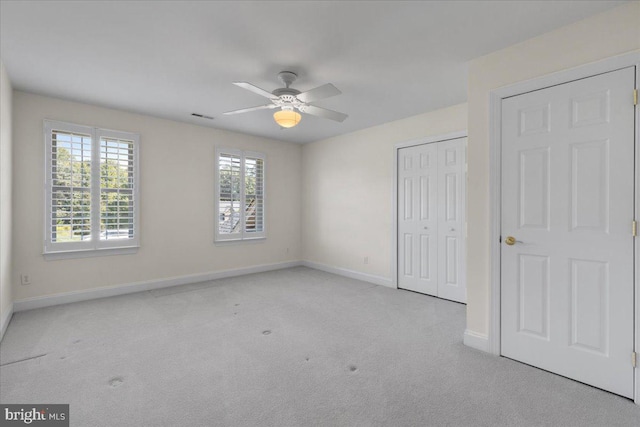 unfurnished bedroom with light colored carpet, multiple windows, and ceiling fan