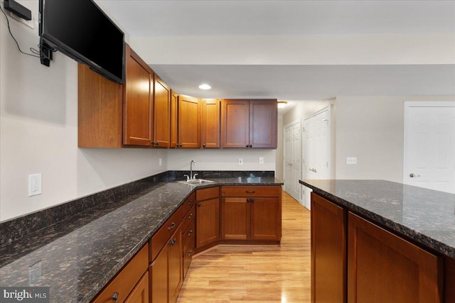 kitchen with light hardwood / wood-style flooring, dark stone countertops, and sink